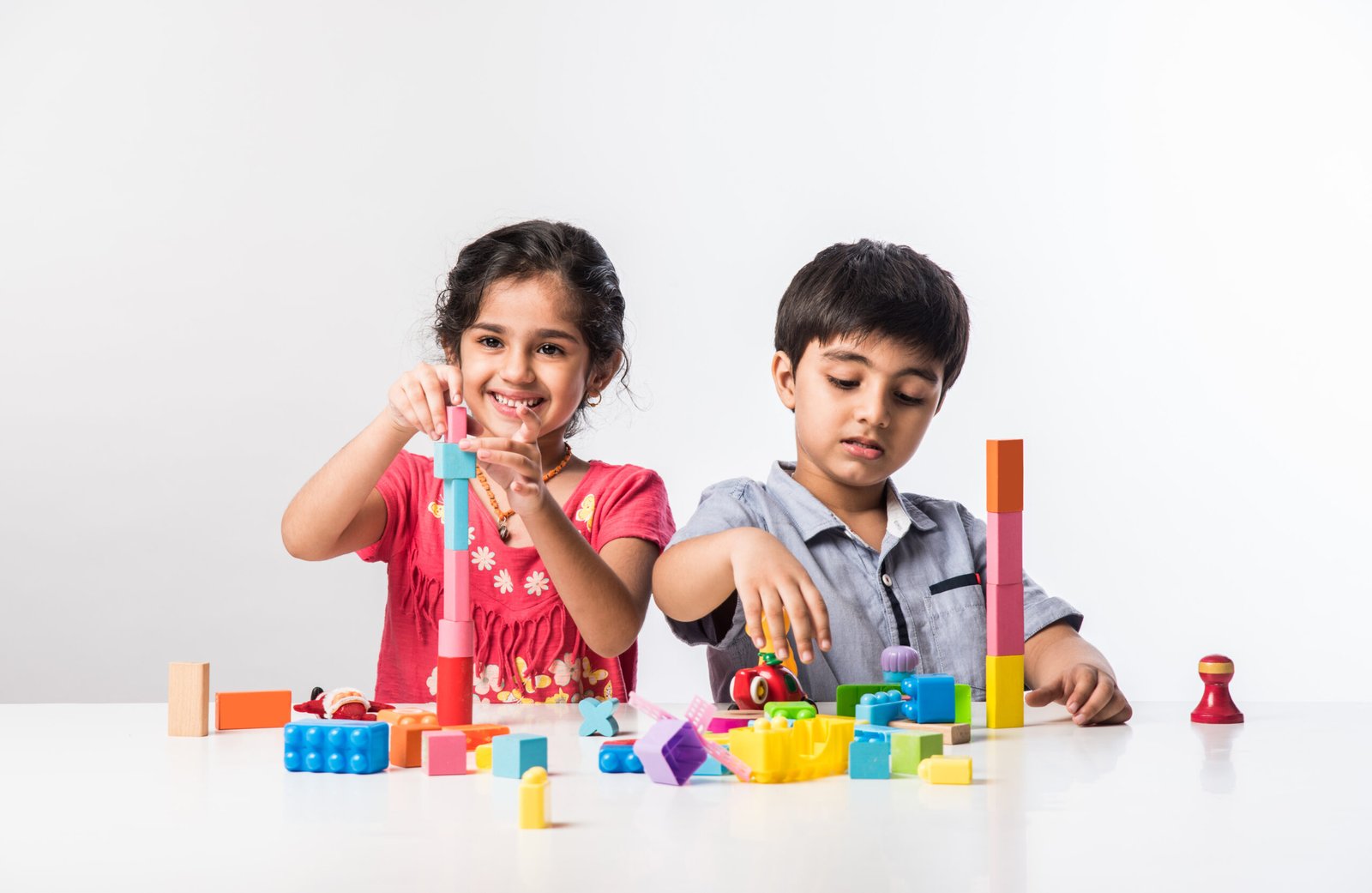 Cute little Indian asian kids playing with colourful plastic toys or blocks while sitting at table or isolated over white background