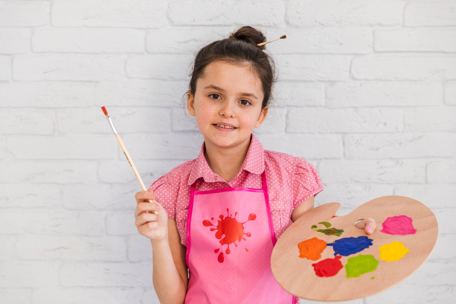 smiling-portrait-girl-standing-against-white-brick-wall-holding-paintbrush-colorful-palette