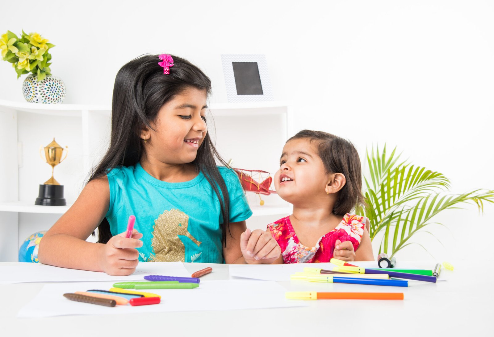 Two Cute little Indian Asian little girls or siblings  enjoying colouring or drawing or painting using pastel colours or sketch pens at table at home