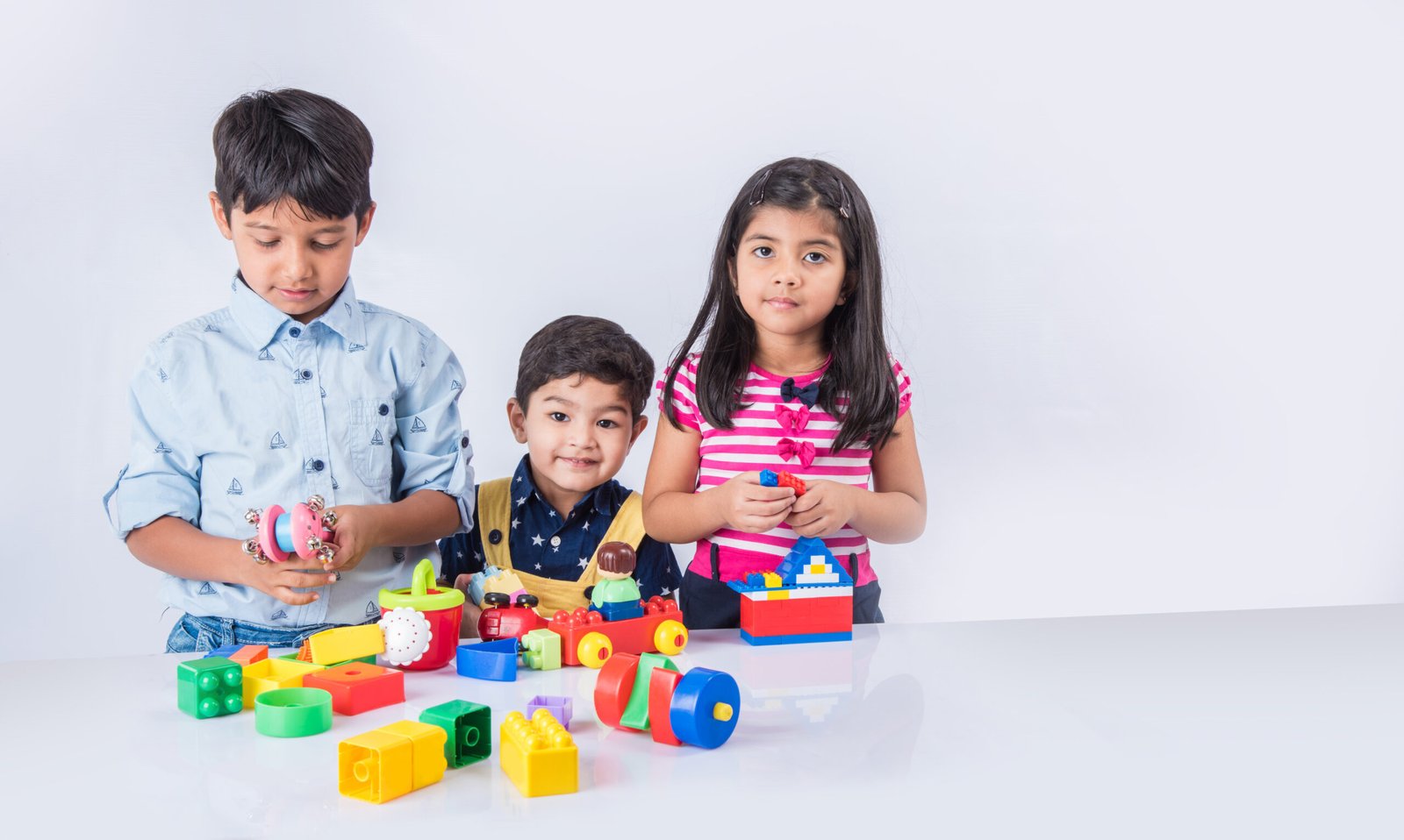 Cute little Indian or asian kids playing with toys or blocks and having fun while sitting at table or isolated over white background