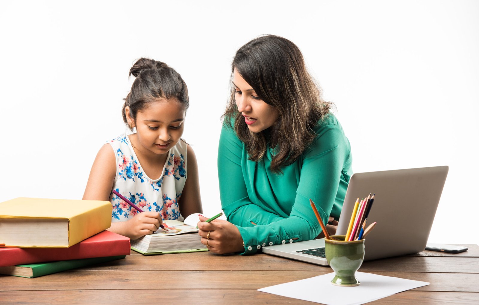 Indian girl studying with mother or teacher at study table with laptop computer, books and having fun learning